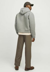 Grau Fleece-Hoodie mit einer Kordelzugkapuze, über einer leichten Schicht getragen, kombiniert mit braunen, weit geschnittenen Hosen und dunklen Schuhen.
