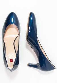 Marintröja lackläders högklackade skor med rund tå, 4 cm blockklack och en röd fyrkantig detalj på innersulan. Slät yta.