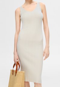 Robe midi en maille côtelée beige clair avec un décolleté en rond et des bretelles fines, associée à un sac en paille texturé avec des poignées marron.