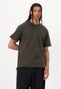 Tricou din bumbac de culoare verde măsliniu, cu mâneci scurte, decolteu rotund și un mic logo Nike embosat pe piept. Textură fină și croială lejeră.