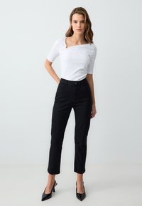 Top bianco a costine con scollatura quadrata e dettaglio rotondo, abbinato a pantaloni in denim neri slim-fit e scarpe nere con tacco alto.