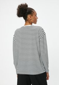 Gestreiftes Langarmshirt in Schwarz und Weiß, aus weichem Material, mit lockerer Passform, rundem Ausschnitt und fallenden Schultern.