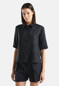 Camicia nera in lino a maniche corte con colletto, sei bottoni frontali e vestibilità rilassata. Texture liscia e design semplice.
