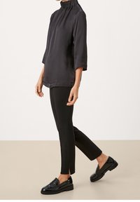 Czarny top z wysokim kołnierzem i rękawami 3/4, zestawiony z czarnymi, dopasowanymi spodniami oraz błyszczącymi czarnymi mokasynami; gładka tkanina, subtelna tekstura i czyste linie.