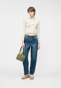 Beige langærmet top med et snoet design, blå høj talje denim jeans, grøn håndtaske med detaljer, og mønstrede beige sko.