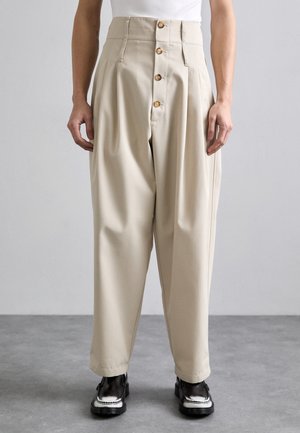 Beige high-waisted trousers with a wide leg, featuring a front button closure, pleats, and a smooth texture. Worn with black shoes.