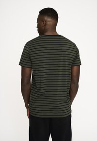 Grøn- og sortstribet t-shirt med korte ærmer og rund hals, lavet af letvægtsstof, vist fra en bagvinkel.
