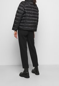 Sort pufferjakke med quiltede sektioner, høj krave og cropped ærmer. Bæres med sorte bukser og kraftige sorte støvler. Glat tekstur.