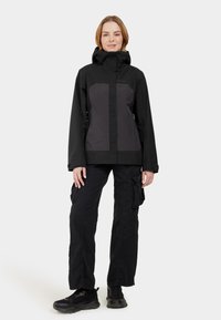 Black waterproof jacket with gray paneling, adjustable hood, and front zipper. Paired with black cargo pants and black athletic shoes.