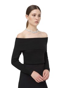 Czarny sweter odsłaniający ramiona, z prążkowanym dekoltem, długimi dopasowanymi rękawami i gładką teksturą, zestawiony z masywnym naszyjnikiem z kryształów.