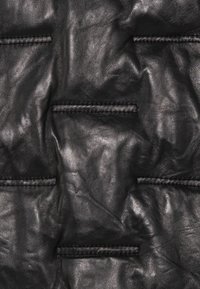 Primer plano de material de cuero negro con patrones rectangulares elevados cosidos y arrugas naturales.