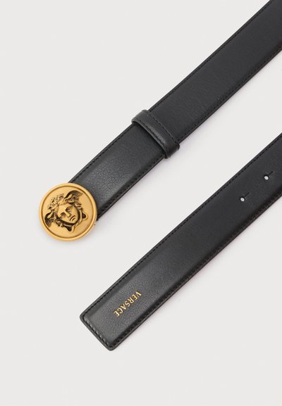Μαύρη δερμάτινη ζώνη Versace με αγκράφα σε σχήμα κεφαλιού Μέδουσας σε χρυσό και χρυσό λογότυπο στο τέλος, τοποθετημένη επίπεδα σε λευκό φόντο.