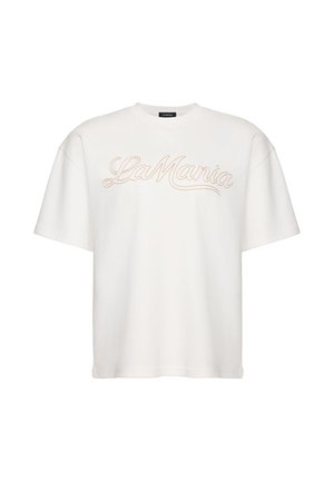 Tricou alb oversized cu mâneci scurte, cu „La Mania” brodat în bej scris cursiv pe piept, guler rotund și o etichetă neagră în interiorul gulerului.