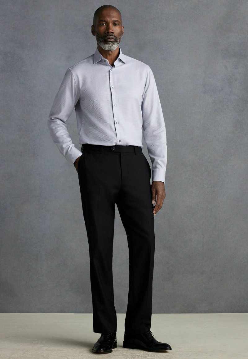 Camisa de botón gris claro con una textura sutil, combinada con pantalones de vestir negros y zapatos negros pulidos. Diseño simple y elegante.