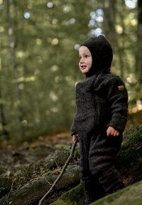 Tumehall villane üheosaline ülikond kapuutsiga, ilma õmblusteta ja esiosal lukuge, mida kannab laps, kes hoiab väljas pulka.