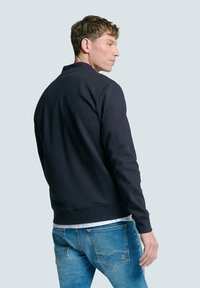 Navyblauwe sweatshirt met een ronde hals en geribbelde manchetten, met een soepele textuur en een relaxte pasvorm, gedragen over lichtblauwe jeans.