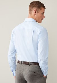 Svetlomodrá košeľa na gombíky s klasickým golierom, s pukmi na chrbte. Kombinovaná so sivými textúrovanými nohavicami a tmavohnedým opaskom.