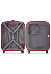 Valigia rossa aperta che mostra un interno a strisce grigie con cinghie elastiche e una tasca con zip. Ruote lisce per la mobilità, forma rettangolare.