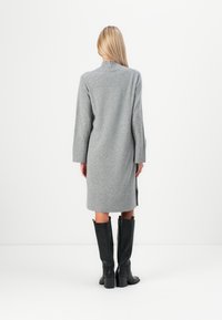 Siva pletena obleka z izrezom, dolgimi rokavi in stranskimi razporki, v kombinaciji z črnimi škornji do kolen. Čist, minimalističen dizajn.