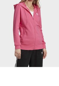Růžová mikina na zip s kapucí, šňůrkami, bočními kapsami a malým bílým logem na hrudi. Měkká tkanina s pohodlným střihem.