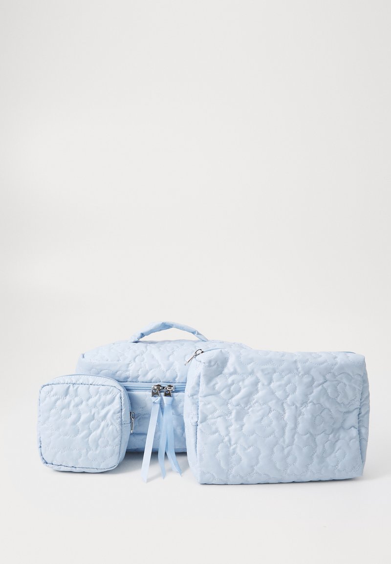 Lyseblå quiltet stof taske sæt, der indeholder en større taske med et top håndtag og to lynlåsposer, prydet med blomsterbroderi.