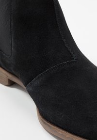 Černé semišové kotníkové boty s elastickými bočními panely a nízkým dřevěným podpatkem. Mají hladký povrch a přesné detaily šití.