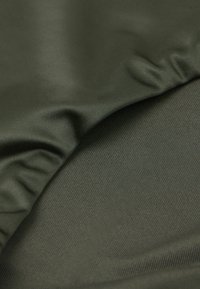 Olivově zelená látka s hladkým povrchem, jemným diagonálním žebrováním a slabými záhyby, což naznačuje pružný materiál vhodný pro oděvy.