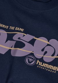 Granatowa tkanina do odzieży sportowej z napisami "hummel SPORTSWEAR," dużym "90's" oraz "SERVE THE GAME" w beżowym i fioletowym kolorze, plus logo pszczoły.