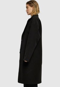 Svart ullfrakk med avslappet passform, lange ermer, oversized silhuett og to frontknapper, som viser en glatt tekstur.