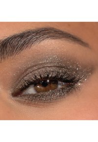 Närbild av ett brunt öga med skimrande taupe ögonskugga, definierade fransar och ett välvårdat mörkt ögonbryn mot en ljus hudton.