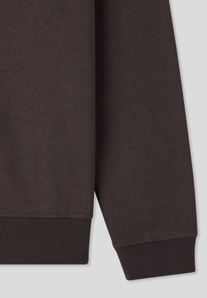 Brązowy długi rękaw bluzy z elastycznymi mankietami i dolnym wykończeniem o prążkowanej teksturze na jasnym tle.