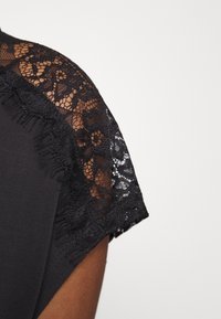 Svart t-shirt med spetsaxlar, blommönster och fransade kanter, som framhäver en kontrasterande textur och design Detalj.