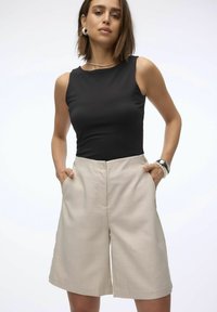 Top negro sin mangas combinado con pantalones cortos plisados beige que cuentan con bolsillos laterales, una textura suave y un ajuste entallado.
