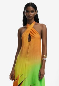 Halterneck dress in gradient orange to green, featuring a keyhole cutout, flowing fabric, and floral accents in the design.