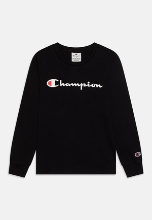 Chemise noire à manches longues avec logo Champion blanc et rouge sur la poitrine et un logo plus petit sur le poignet gauche.