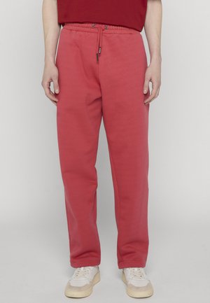 Person wearing red drawstring sweatpants and white sneakers standing against a plain light background.