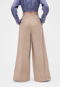 Beiget leveälahkeiset puuvillahousut, joissa on korkea vyötärö, kaksi takataskua ja siisti lahkeenreuna.