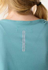 Maglietta a maniche corte color turchese chiaro con un motivo a griglia testurizzato e un logo verticale "SWEDEMOUNT" in stampa riflettente sulla schiena.