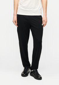 Μαύροι παντελόνες από μαλακό υλικό, με άνετη εφαρμογή, με στενότερα πόδια και μικρό λογότυπο στη αριστερή πλευρά.