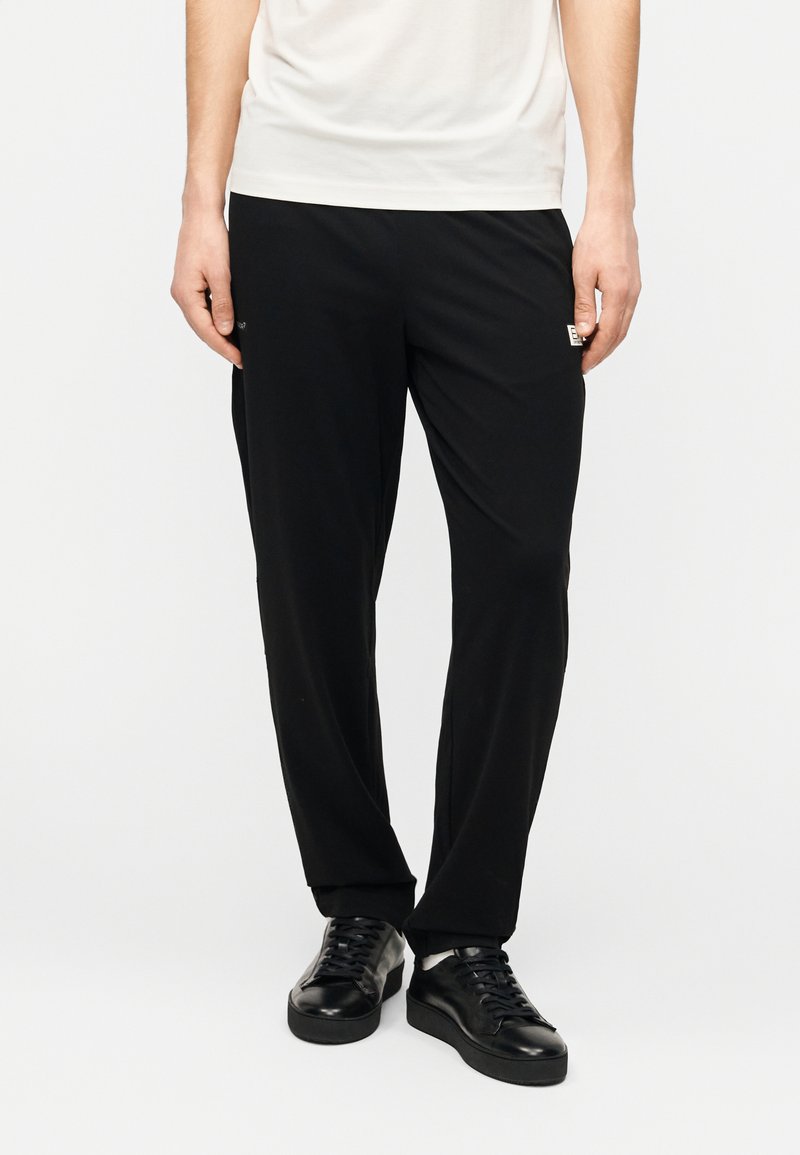 Μαύροι παντελόνες από μαλακό υλικό, με άνετη εφαρμογή, με στενότερα πόδια και μικρό λογότυπο στη αριστερή πλευρά.