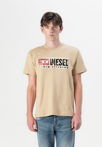 Bežinis medvilninis marškinėlis su nusidėvėjusiu juodu ir raudonu „Diesel“ grafiniu ženklu priekyje. Trumpomis rankovėmis ir klasikinio apvalaus kaklo dizainu.