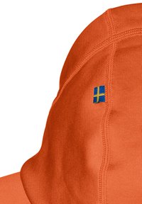 Orange kasket fremstillet af tekstureret stof, med et lille blå og gult patch. Designet indeholder synlige stikninger og en buet skygge.