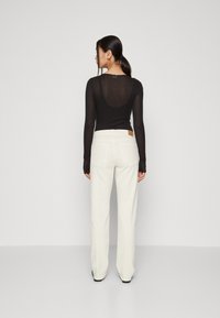 Top negro de manga larga con escote en la espalda, combinado con pantalones anchos de tiro alto en blanco que cuentan con dos bolsillos traseros y una etiqueta de marca.