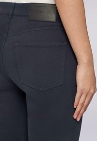 Tmavě námořnické džíny s koženou značkou, designem pěti kapes a tvarovanou zadní kapsou, a hladkou, elastickou texturou látky.