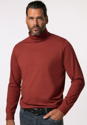 Rustfarbener Rollkragenpullover aus glattem Material mit langen Ärmeln und figurbetonter Passform. Kombiniert mit blauen Jeans und einem schwarzen Gürtel.