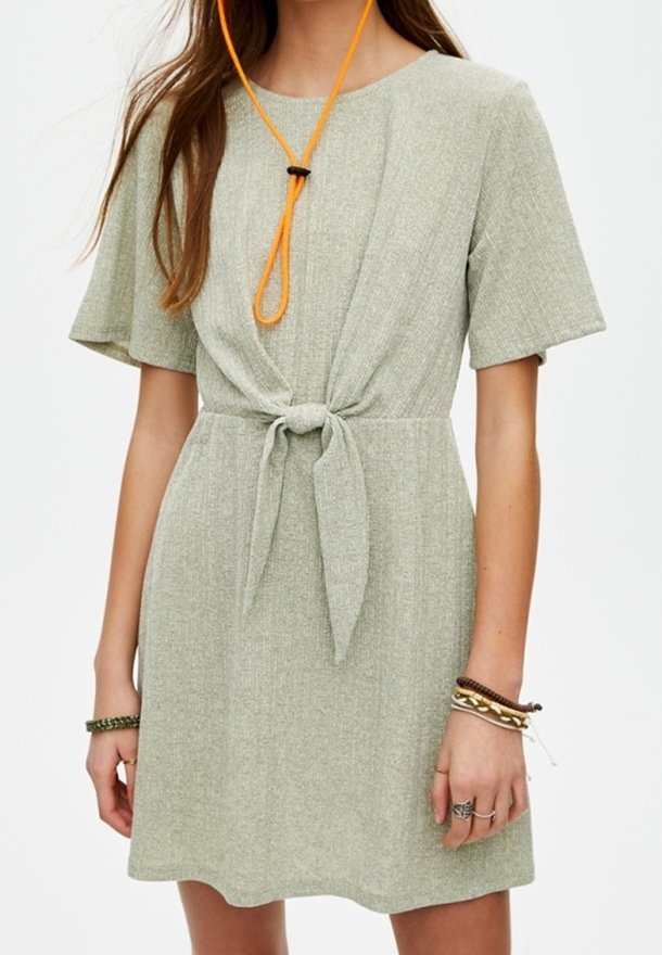 Femme portant une robe gris clair à manches courtes avec un nœud à l'avant et des bracelets superposés sur son poignet droit.