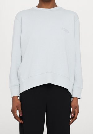 Lyseblå sweatshirt med ribbet kant og manchetter. Har en afslappet pasform og et lille grafisk detalje på brystet. Glat tekstur og afslappet design.