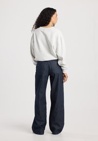 Gray sweatshirt with dropped shoulders and a relaxed fit paired with wide-leg, navy corduroy pants featuring vertical stripes.