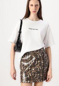 Witte oversized t-shirt met zwarte tekst, gecombineerd met een metallic minirok met luipaardprint. Zwarte handtas met een schouderriem.