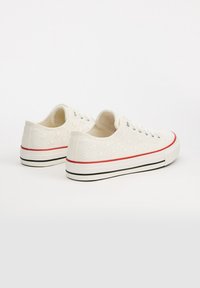 Zapatillas de lona blancas con un patrón floral, cordones grises y una franja roja en la suela. Diseño de corte bajo con suela de goma.